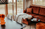 Knusse woonkamer in de Klapkot-cabine met een bruine zetel, eettafel en grote ramen naar de natuur.