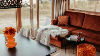 Acogedora sala en la cabaña Klapkot con sofá marrón, manta suave, mesa de comedor y amplios ventanales.