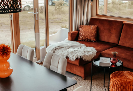 Acogedora sala en la cabaña Klapkot con sofá marrón, manta suave, mesa de comedor y amplios ventanales.