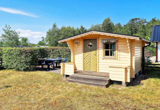 Small yellow wooden cabin with porch and outdoor seating, located in Skummeslövsstrand, Sweden.