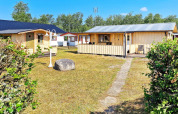 Sommerhus i Skummeslövsstrand, Sverige, med gulmalede træhytter, terrasse og grøn have under blå himmel.