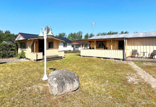 Feriehytte i Skummeslövsstrand, Sverige, med flere bygninger, have og udendørs siddepladser i solskin.