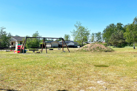 Legeplads med gynger og legeredskaber ved feriehus i Skummeslövsstrand, Sverige, under blå himmel.