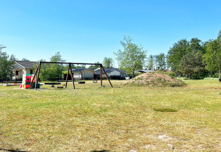 Legeplads med gynger og legeredskaber ved feriehus i Skummeslövsstrand, Sverige, under blå himmel.