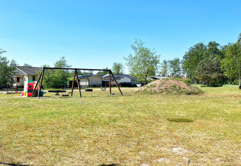 Spielplatz mit Schaukeln und Spielgeräten am Ferienhaus in Skummeslövsstrand, Schweden, bei sonnigem Wetter.