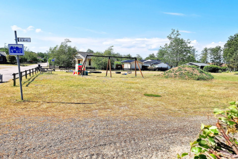 Spielplatz mit Schaukeln und Rutsche neben Ferienhaus in Skummeslövsstrand, Schweden an einem sonnigen Tag.