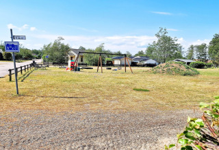 Parque infantil con columpios y tobogán junto a casa vacacional en Skummeslövsstrand, Suecia, en un día soleado.