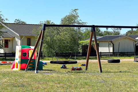 Playground with swings and playhouse near lodges in Skummeslövsstrand, Sweden, on a sunny day.