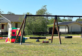 Parque infantil con columpios y casita de juegos frente a cabañas en Skummeslövsstrand, Suecia, al sol.