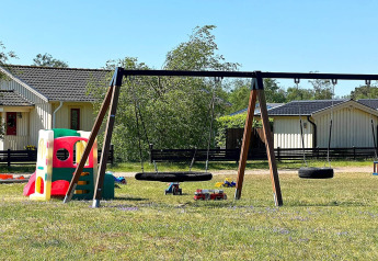 Aire de jeux avec balançoires et maisonnette devant des lodges à Skummeslövsstrand, Suède, par beau temps.