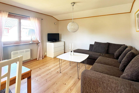 Lyst opholdsstue i en feriebolig i Skummeslövsstrand, Sverige, med hjørnesofa, tv og stort vindue.