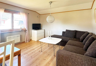 Bright living room at a holiday home in Skummeslövsstrand, Sweden, featuring a corner sofa, TV, and window.