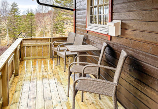 Gezellig balkon bij een houten yurt met rotan stoelen, tafel en uitzicht op het bos in Lysøysundet.