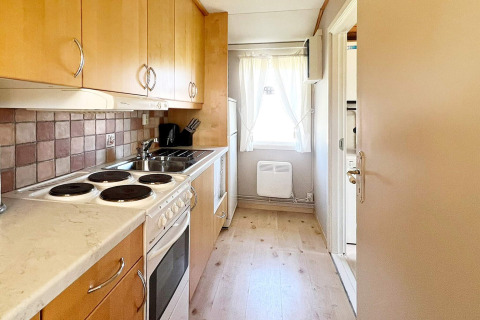 Cocina compacta con estufa eléctrica, armarios de madera y ventana en alojamiento de Skummeslövsstrand, Suecia.