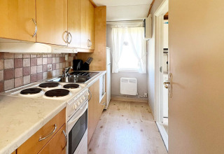 Piccola cucina con forno elettrico, mobili in legno e finestra in una casa vacanze a Skummeslövsstrand, Svezia.