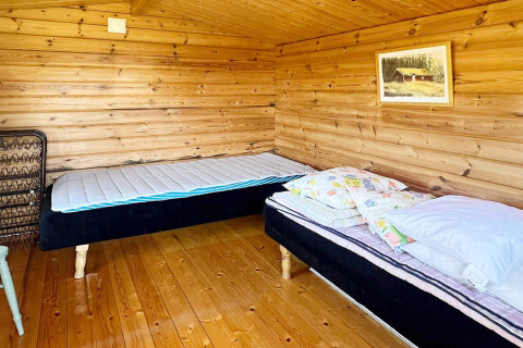 Habitación de cabaña de madera con dos camas individuales, suelo de madera y cuadro, en Skummeslövsstrand.