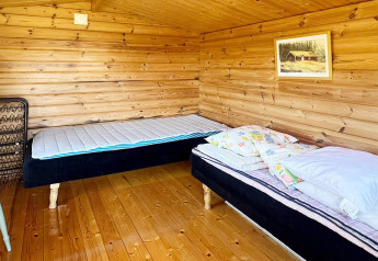 Cozy wooden lodge bedroom with two single beds, wood floor, and artwork on the wall in Skummeslövsstrand.