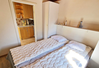 Dormitorio con dos camas individuales, armario blanco y vista a la cocina en casa vacacional en Skummeslövsstrand, Suecia.