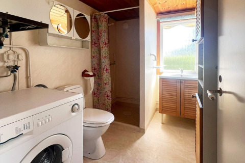 Badeværelse med vaskemaskine, toilet, bruser med farverig forhæng og vindue i feriehus i Skummeslövsstrand.