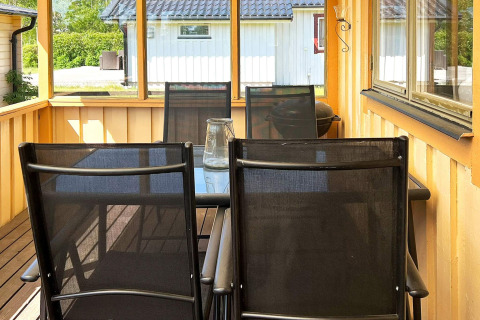 Overdekt terras met glazen tafel en vier zwarte stoelen bij een vakantieverblijf in Skummeslövsstrand, Zweden.