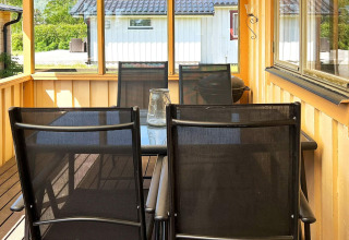 Portico coperto con tavolo in vetro e quattro sedie nere in una casa vacanze a Skummeslövsstrand, Svezia.