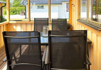 Portico coperto con tavolo in vetro e quattro sedie nere in una casa vacanze a Skummeslövsstrand, Svezia.