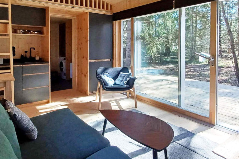 Lichte moderne woonkamer in een cabin met grote ramen, terras en boszicht in Höllviken, Zweden.