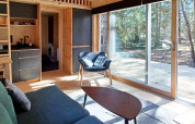 Salon lumineux et moderne d’un chalet avec grandes baies vitrées sur terrasse et forêt à Höllviken, Suède.