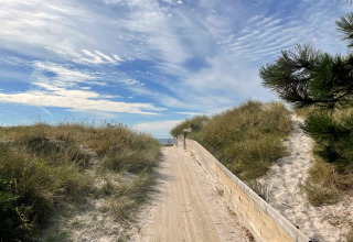 Passerelle en bois traversant les dunes vers la plage à Höllviken, Suède, sous un ciel bleu nuageux.