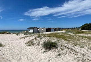 Feriebadehytter på sandstrand i Höllviken, Sverige, med klitter, græs og blåt hav under klar himmel.