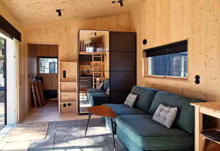 Chalet moderne en bois à Höllviken, Suède, avec canapé vert, grande fenêtre et armoire miroir.