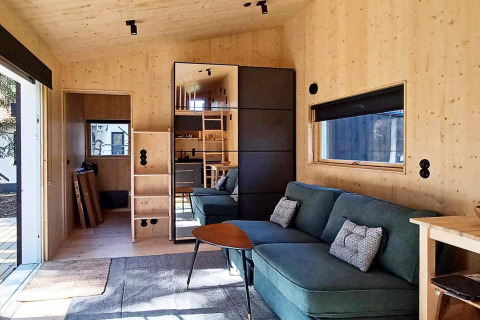 Moderna casa vacanze in legno a Höllviken, Svezia, con divano verde, finestra ampia e armadio a specchio.