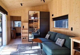 Modernes Ferienhaus in Höllviken, Schweden, mit Holzinterieur, grüner Couch und großem Fenster.
