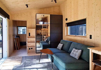 Modernes Ferienhaus in Höllviken, Schweden, mit Holzinterieur, grüner Couch und großem Fenster.