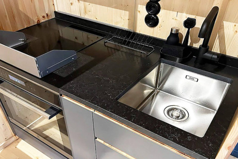 Moderne spoelbak en oven met zwart aanrechtblad in hut in Höllviken, Zweden, houten wand.