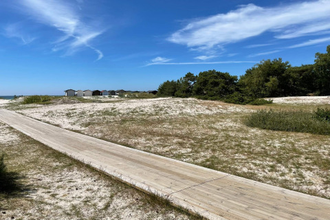 Promenade en bois à travers les dunes de sable et cabanes de plage sous ciel bleu à Höllviken, Suède.