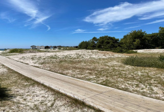 Houten pad over zandduinen en strandhuisjes onder een blauwe lucht in Höllviken, Zweden.