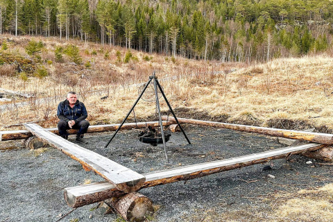Uomo seduto vicino a un focolare recintato da tronchi, nei pressi di una yurta a Lysøysundet, Svezia.