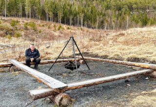 Man zit bij een vuurplaats met houten omlijsting naast een yurt in Lysøysundet, Zweden, vlakbij het bos.