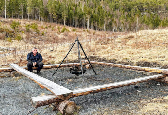 Man zit bij een vuurplaats met houten omlijsting naast een yurt in Lysøysundet, Zweden, vlakbij het bos.