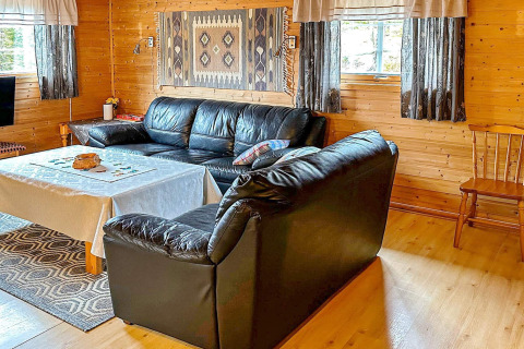 Soggiorno accogliente con divani in pelle nera, pareti di legno e finestra con tende a Lysøysundet.