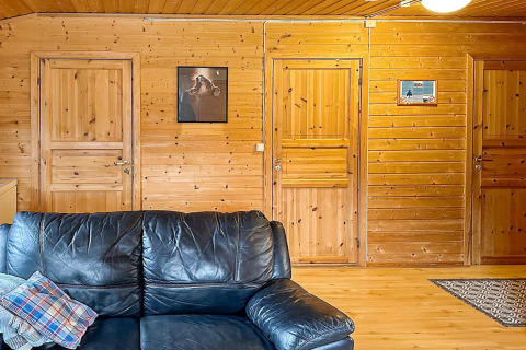 Salon lambrissé de bois dans une yourte suédoise avec canapé en cuir noir, trois portes et décor mural.