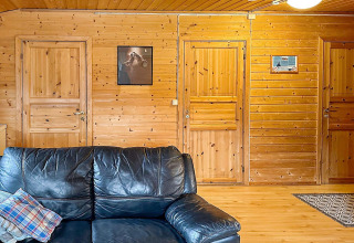 Soggiorno con pareti in legno in una yurta svedese, divano nero in pelle e tre porte in legno.