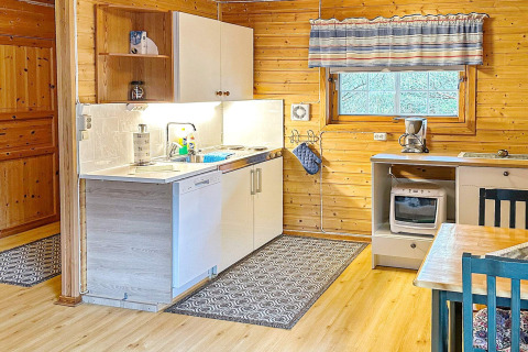 Gemütliche Küche in einer Blockhütte mit modernen Geräten, Holzwänden und gestreiften Vorhängen.