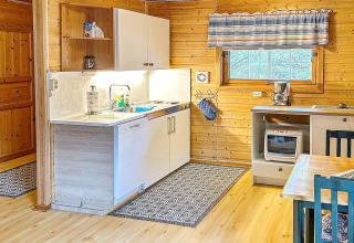 Cuisine chaleureuse dans une maison de vacances en bois avec équipements modernes et rideaux rayés.