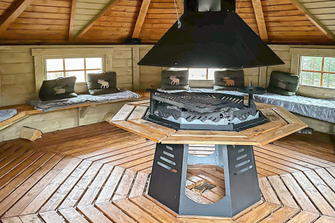 Interior of a cozy round yurt with wooden benches, pillows, and a central fireplace in Lysøysundet, Sweden.