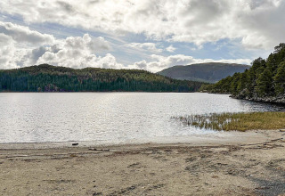 Lake with sandy shore, forested hills and cloudy sky near 4-person yurt in Lysøysundet, Sweden.