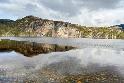 Foto de un lago tranquilo con agua cristalina y montañas reflejadas, tomada cerca de una yurta en Lysøysundet, Suecia.