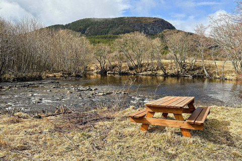 Picknicktafel aan de rivier met kale bomen en een beboste berg op de achtergrond in Lysøysundet, Zweden.