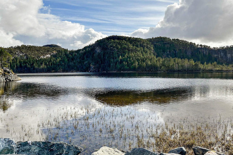 Vue d’un lac calme reflétant des collines boisées et un ciel dramatique, depuis une yourte à Lysøysundet, Suède.